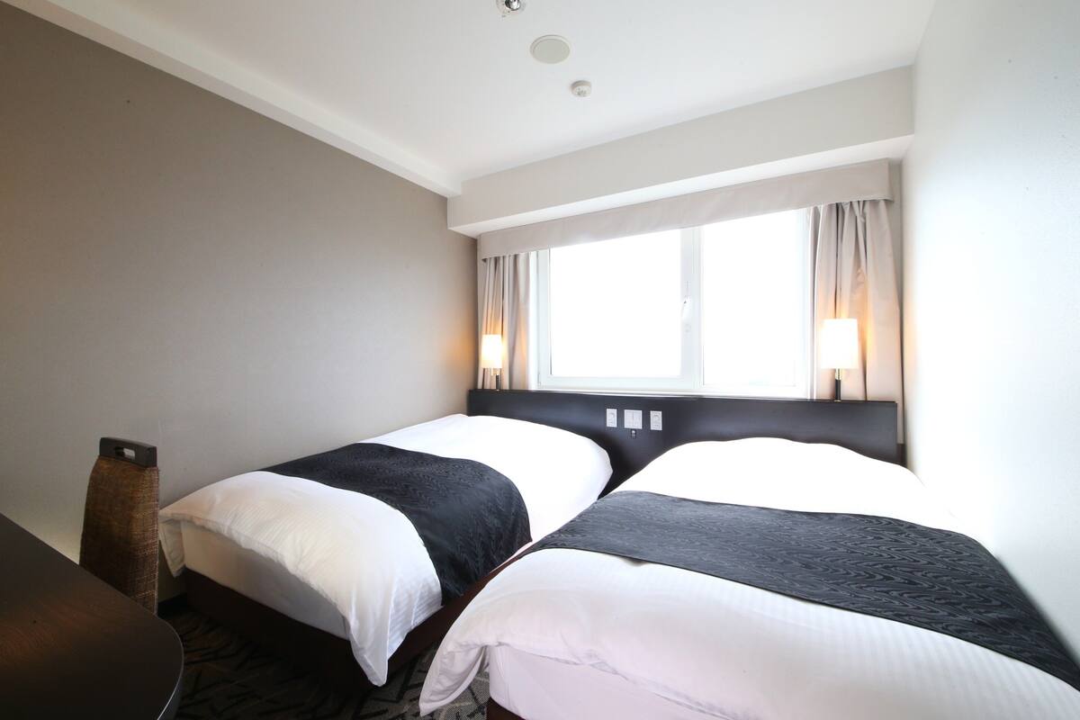 Ett hotellrum med två sängar, ett skrivbord och ett fönster med gardiner.