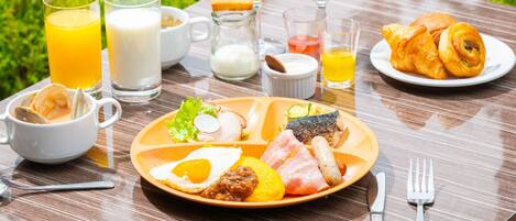 Una mesa de desayuno con diversos alimentos, entre ellos huevos, jamón y croissants, además de bebidas y condimentos.