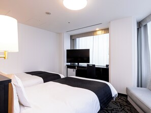 A hotel room with two beds, a desk with a TV, and a seating area.