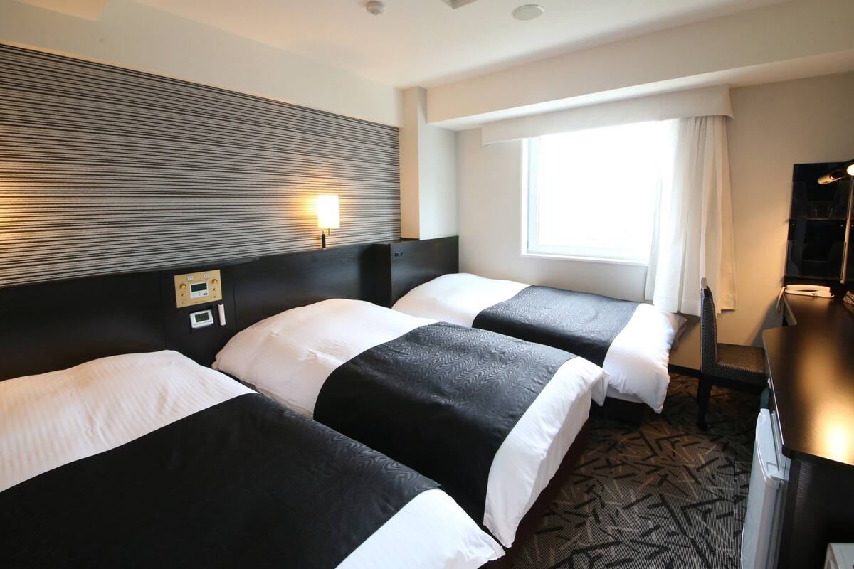 Ett hotellrum med två sängar, ett skrivbord, en stol, en TV och ett fönster med gardiner.