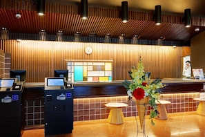 A reception area with a wooden panel wall, a clock, a reception desk, and a flower arrangement. - Hotel Ranpu (Hirado-shi)