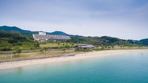 A coastal hotel with a large building, a beach, and mountains in the background. - Hotel Ranpu (Hirado-shi)