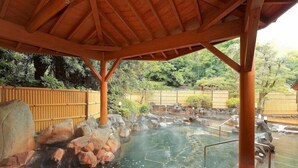A traditional Japanese onsen with a wooden pavilion, a stone hot spring, and a bamboo fence in the background. - Hotel Ranpu (Hirado-shi)