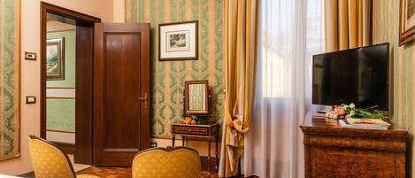 A hotel room with a wooden floor, a bed, a TV on a wooden stand, a desk with a mirror, and a chair.