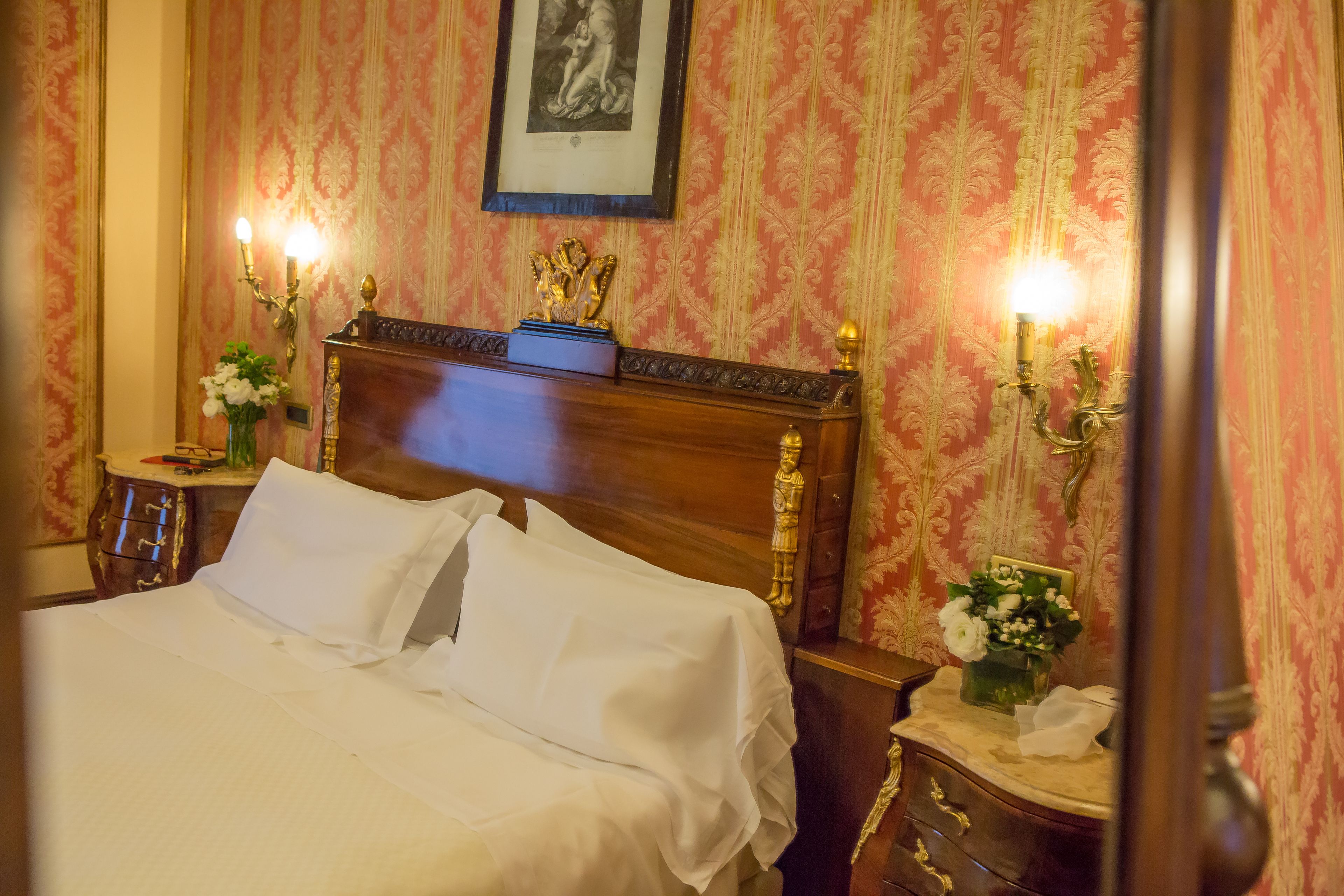A hotel room with a large bed, ornate headboard, and decorative wall sconces.