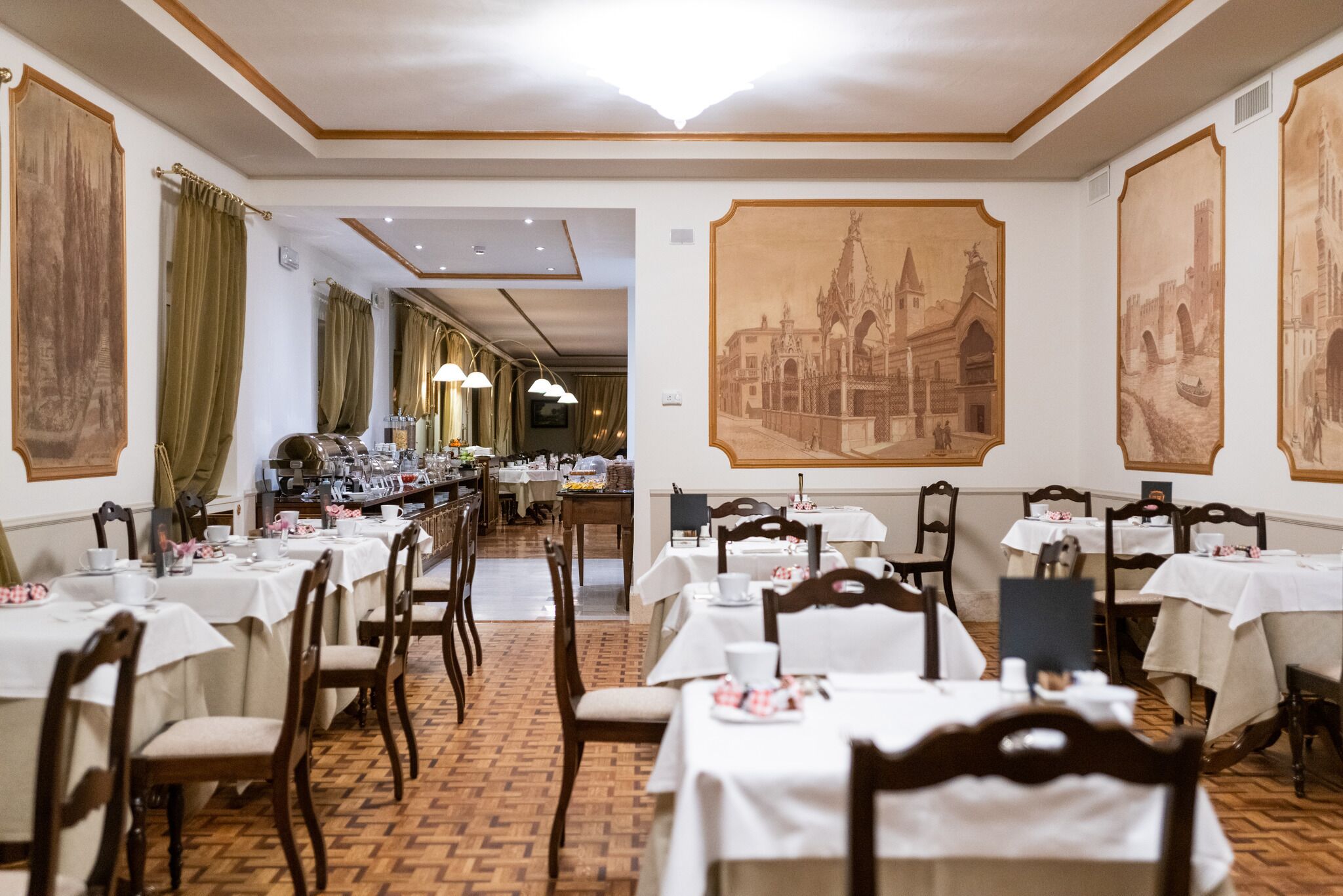 Un comedor con mesas dispuestas para el servicio, sillas de madera y grandes cuadros en las paredes.