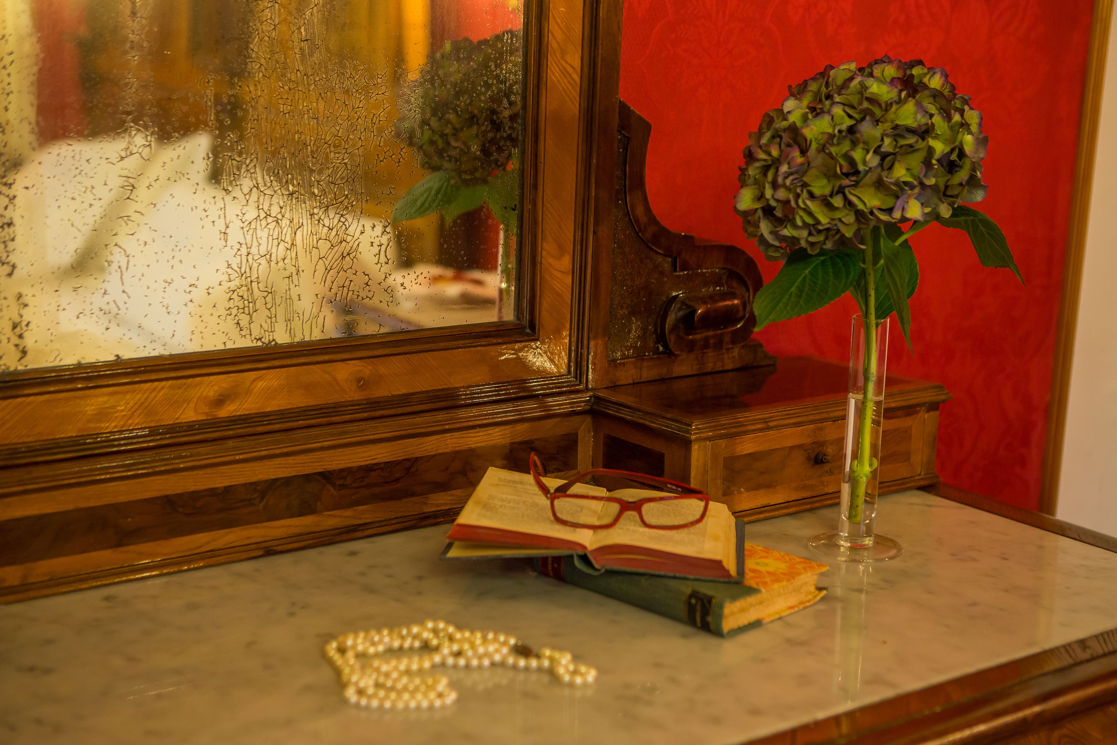 Une table en bois sur laquelle se trouvent un livre, une paire de lunettes, un vase avec une fleur et un collier de perles.