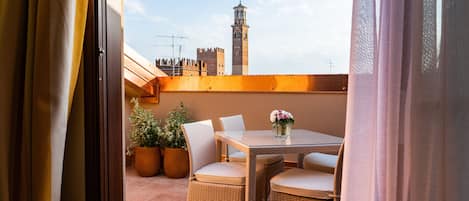 A balcony with wicker furniture, potted plants, and a view of a historic tower.