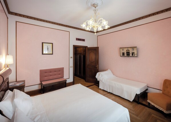 A hotel room with two beds, a sitting area, a chandelier, and a door leading to another room.