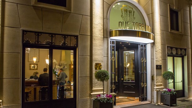 A hotel entrance with a dark door, a reception desk, and two potted plants.