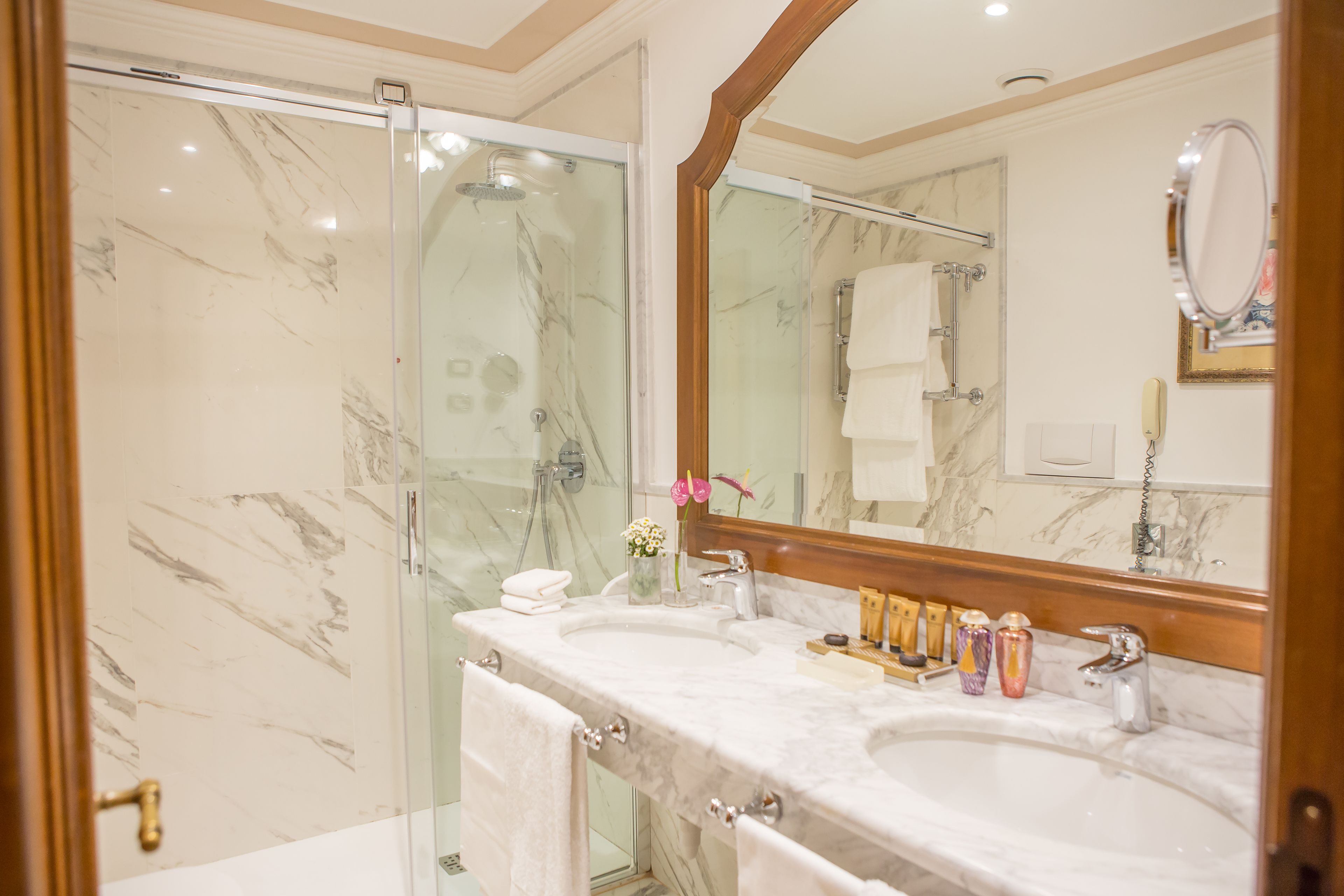 Une salle de bain dotée d’une douche en verre, de deux lavabos, d’un grand miroir et de murs en marbre.