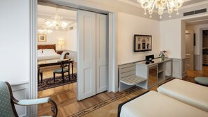 A hotel room with a bed, a desk, a chair, a chandelier, and a mirror on the wall.