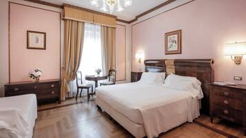A hotel room with a large bed, a desk with a chair, a small table with a vase of flowers, and a nightstand with a lamp.