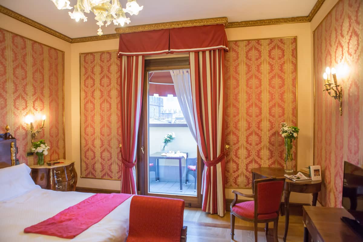 A hotel room with a large bed, a desk, a chair, and a view of the outside.
