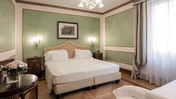 Un dormitorio ordenado con una cama grande, una mesita de noche con un florero, un cuadro en la pared y una araña.