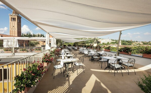 An outdoor terrace with tables and chairs, a white canopy, and a view of a historic building in the background.