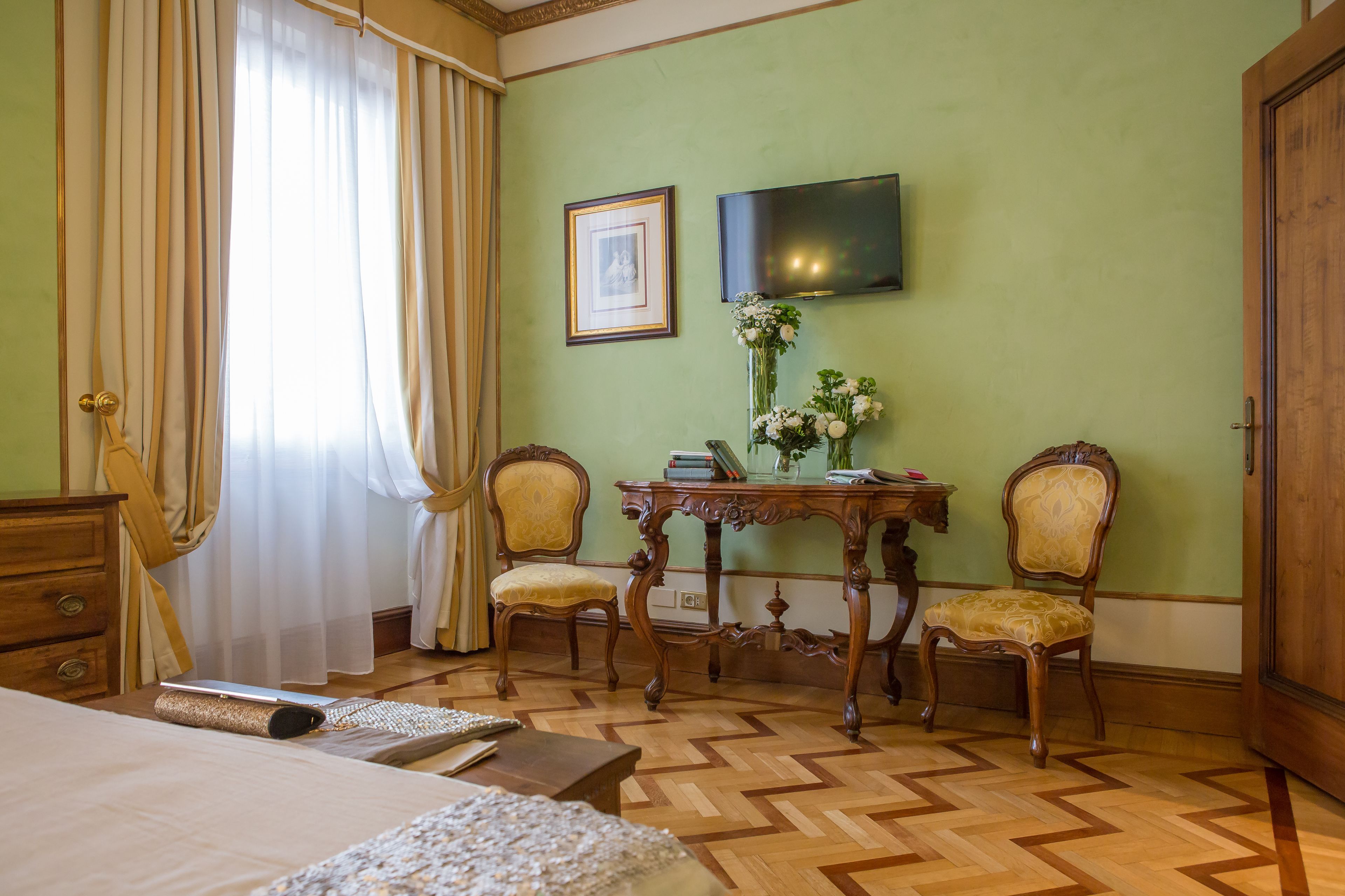 A hotel room with a bed, a desk with a chair, a TV, and a wooden wardrobe.