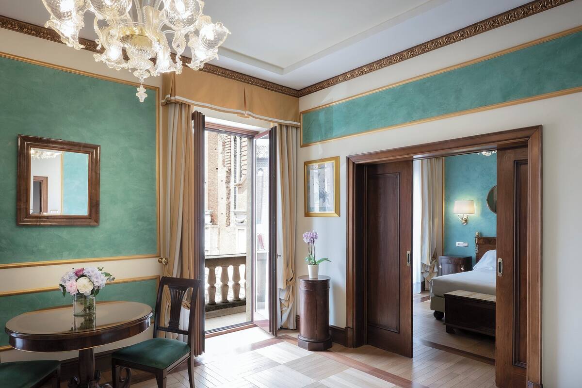 A hotel room with a dining area, a chandelier, a view of the city, and a bed.