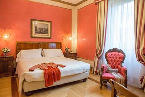 A hotel room with a large bed, a wooden nightstand, a red armchair, and a framed picture on the wall.
