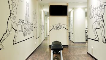 Un gimnasio con equipo de ejercicio y paredes decoradas con grabados lineales.