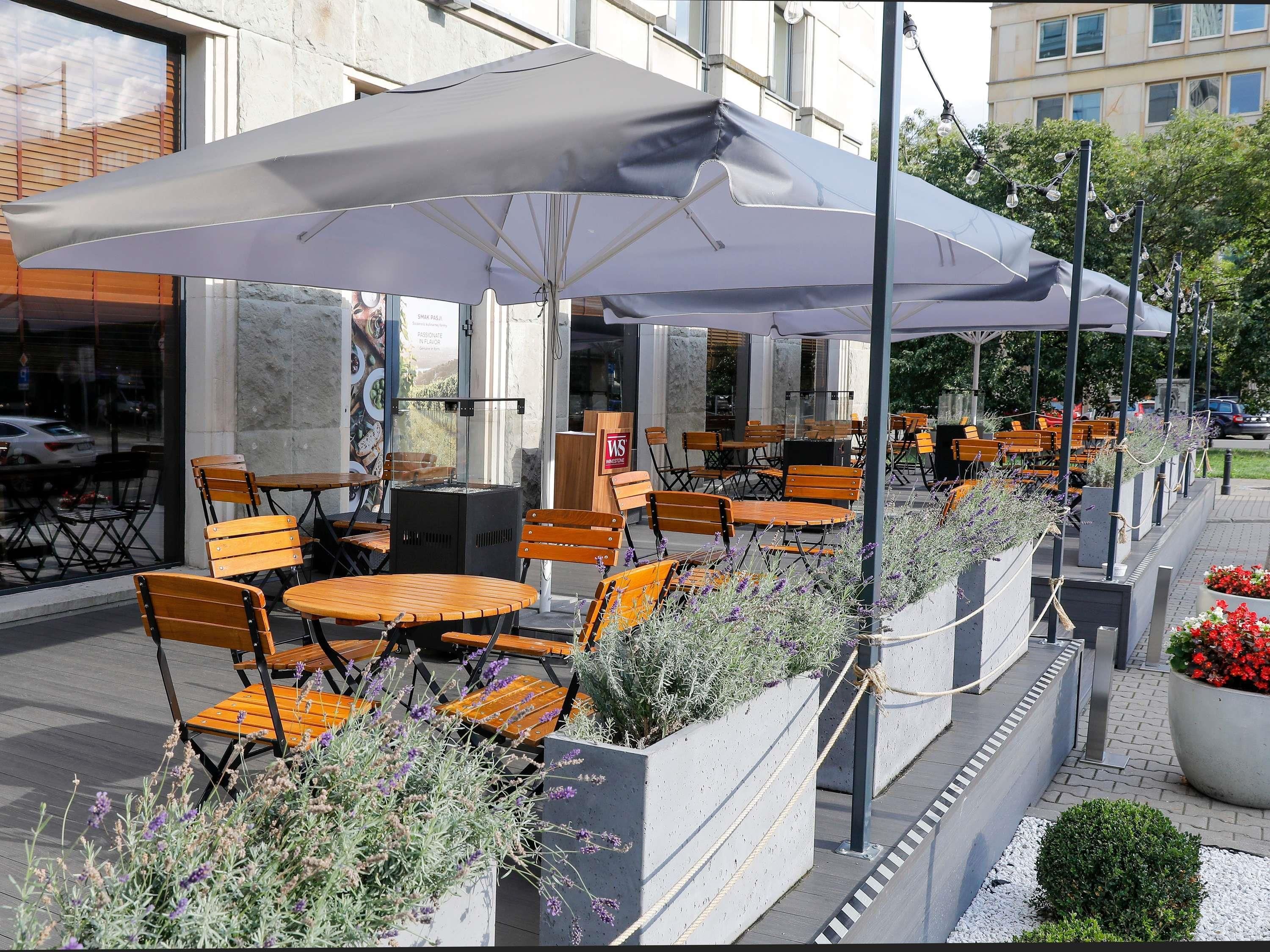 Espace extérieur aménagé avec des tables et des chaises, un espace couvert avec un parasol, et des jardinières décoratives avec des fleurs.