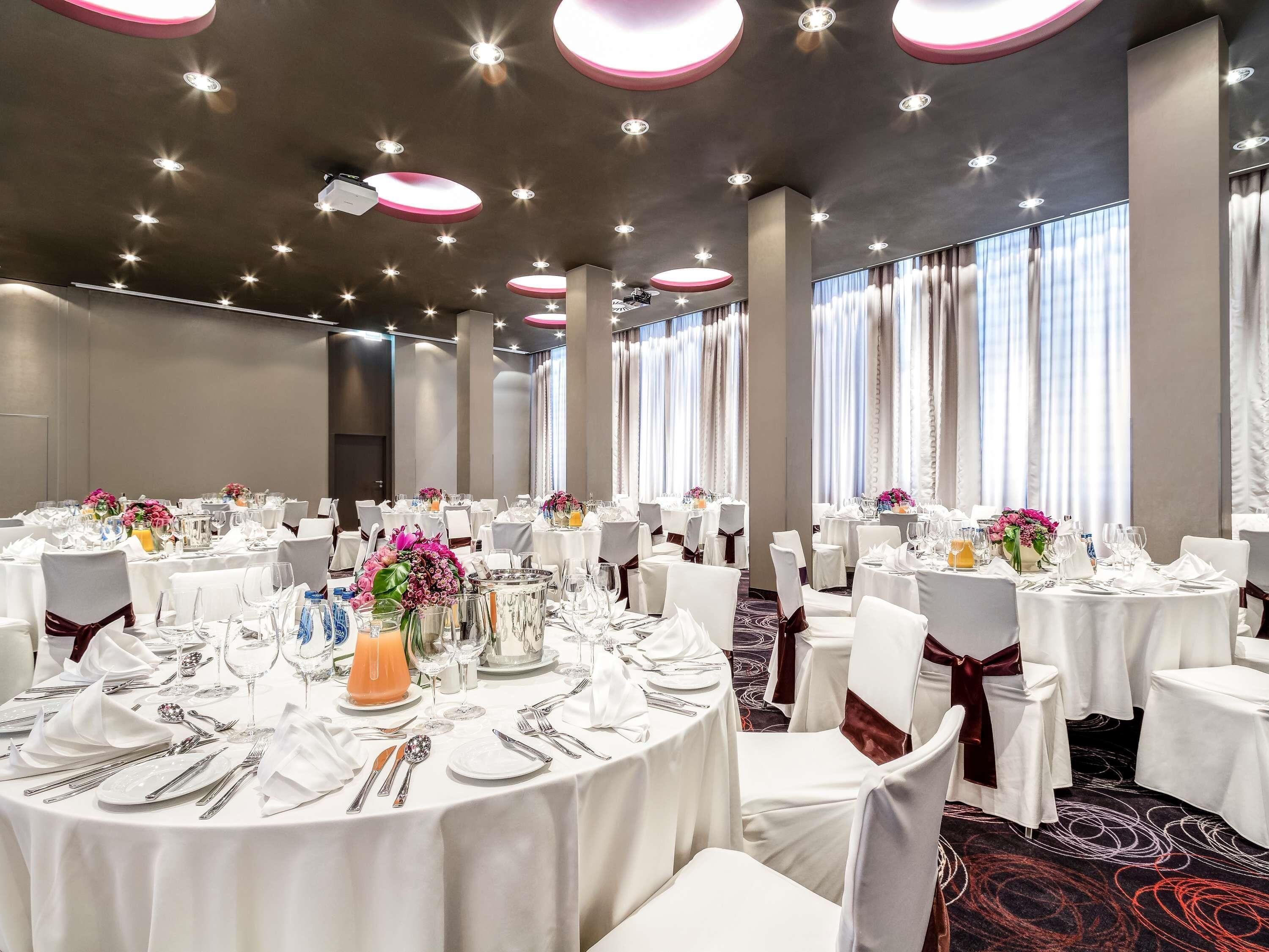 Une salle de banquet avec des tables rondes, des nappes blanches et des chaises recouvertes de housses blanches.