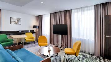 Habitación de hotel con sofá, sillas, una mesita, televisor y alfombra estampada.