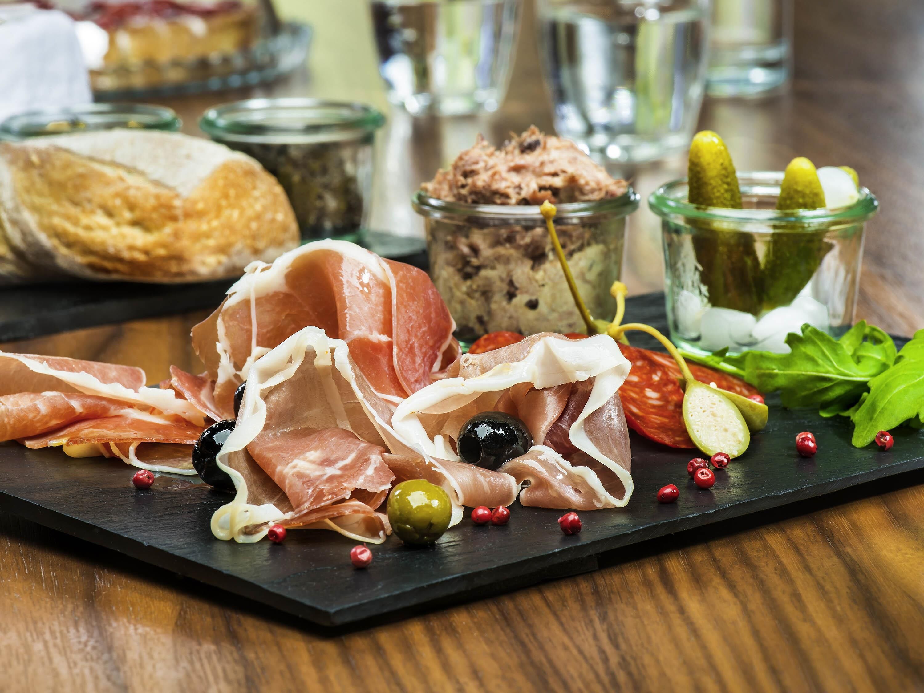 A charcuterie board with various meats, olives, and pickles.