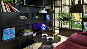 A modern room with a black bookshelf, gaming console, and a round table with two controllers. - Mercure Warszawa Grand (Warsaw)