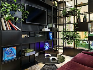 Una camera moderna con una libreria nera, una console di gioco e un tavolo rotondo con due comandi.