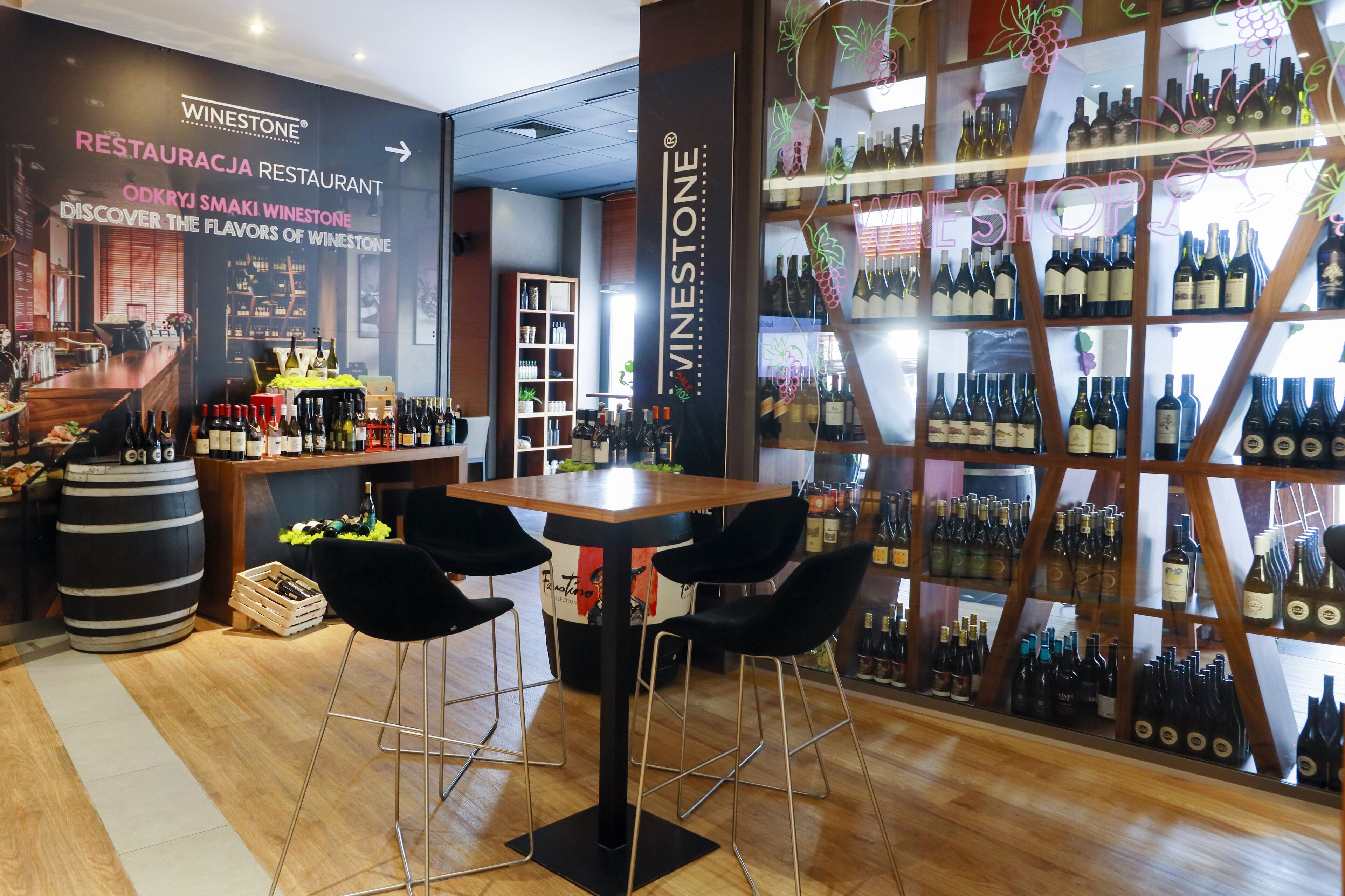 A wine shop interior with a bar area, wooden shelves with wine bottles, and a counter with wine glasses.