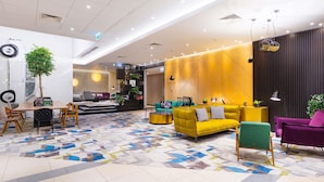 A modern hotel lobby with a dining area, seating, and a decorative wall. - Mercure Warszawa Grand (Warsaw)