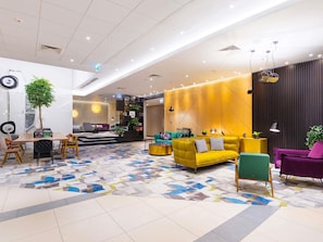 Una hall d'albergo moderna con area ristorazione, posti a sedere e una parete decorativa.