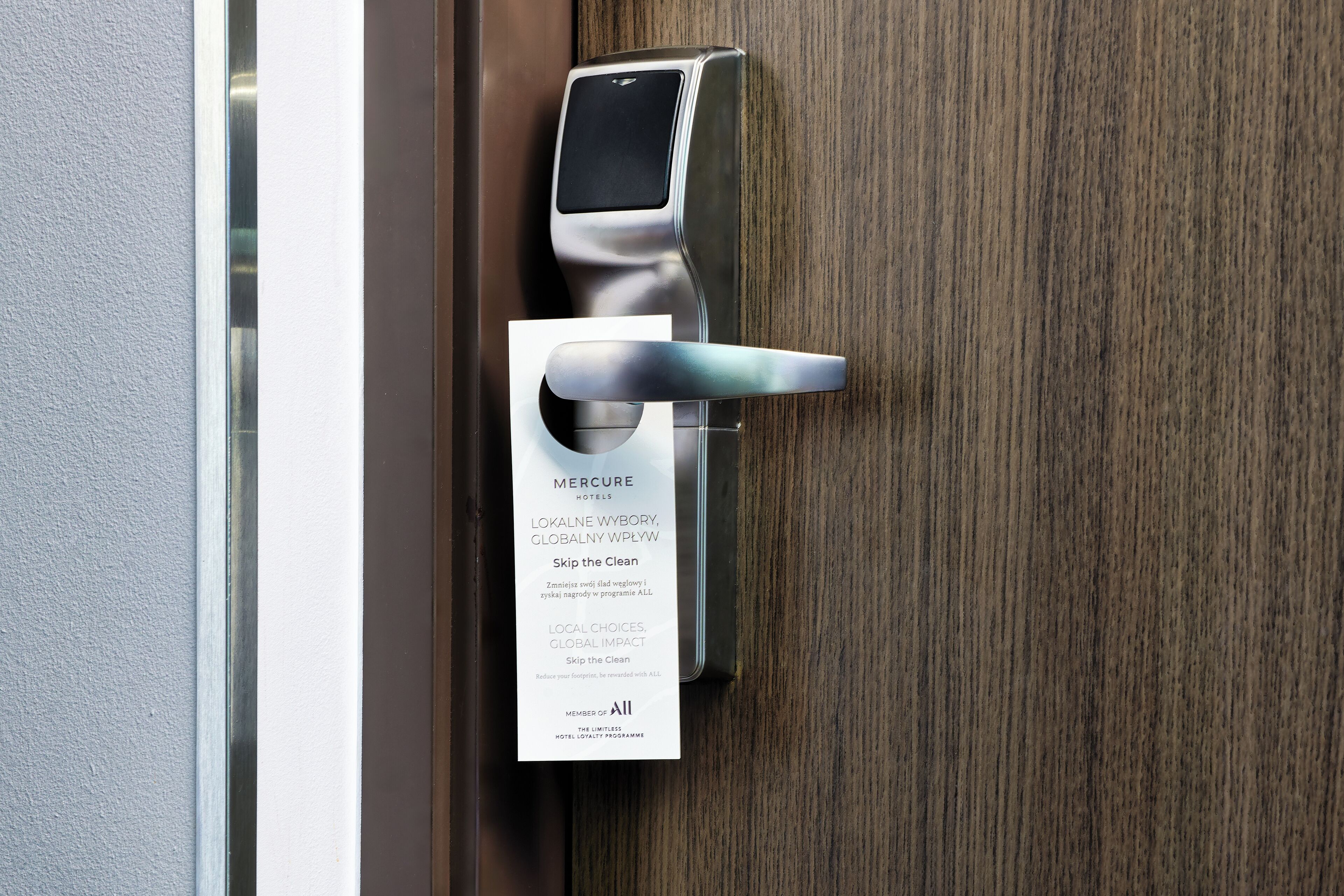 A modern hotel door with a digital keycard reader and a sign indicating membership in the 'Skip the Clean' program.