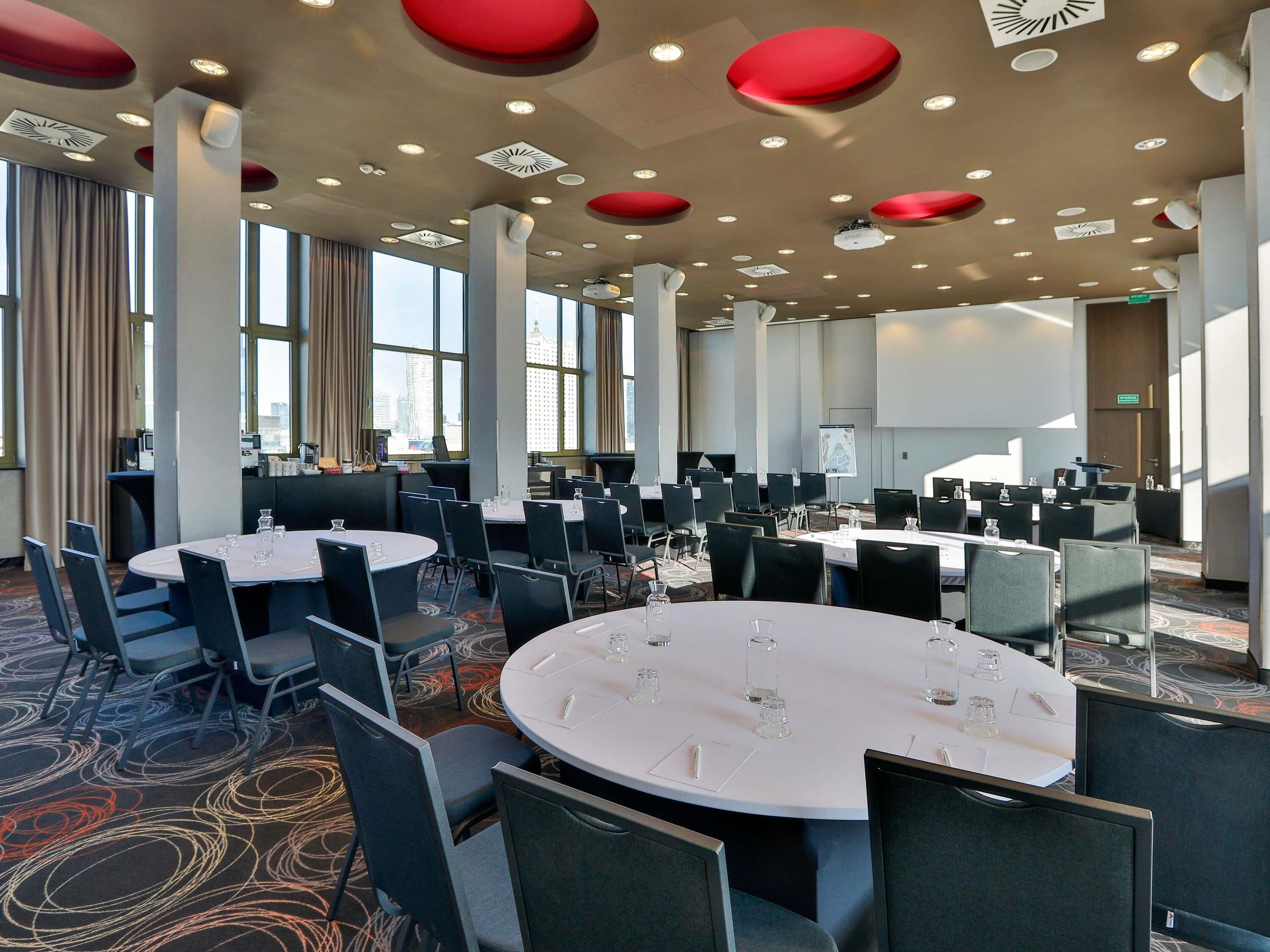 Une salle de conférence dotée de plusieurs tables rondes, de chaises noires et d’un sol recouvert de moquette.