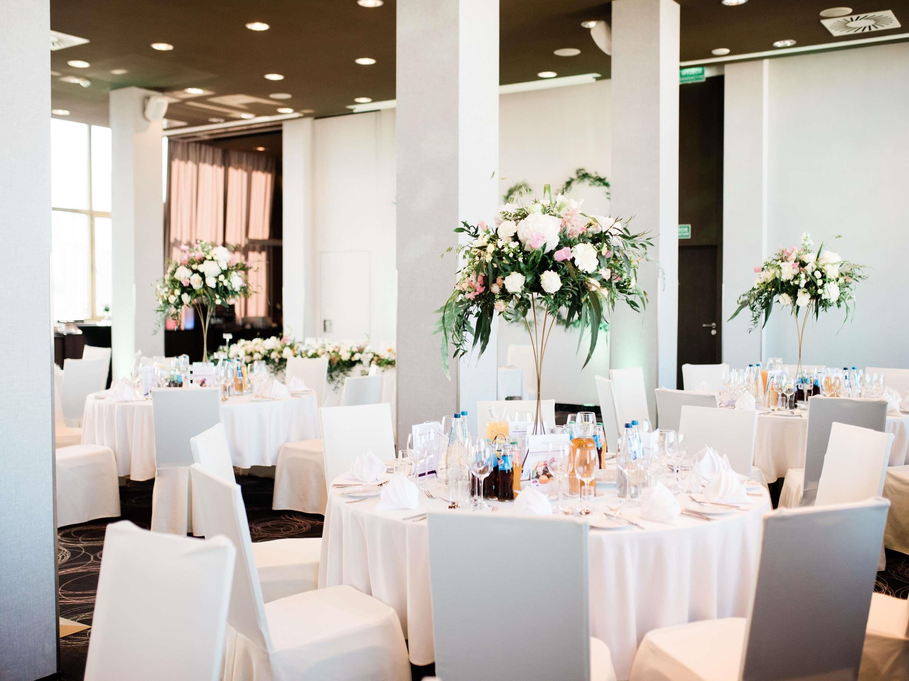 A banquet hall with round tables set for a formal event, each with floral centerpieces and glassware.