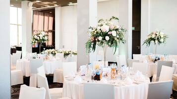 Un salón de banquetes con mesas redondas dispuestas para un evento formal, cada una con centros de mesa florales y cristalería.