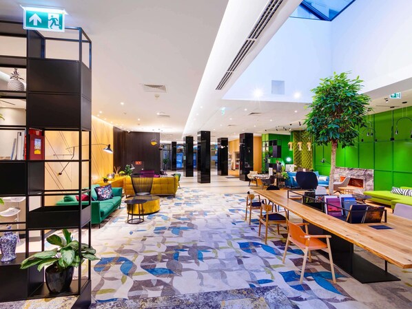 Un hall d’entrée moderne avec un comptoir d’accueil, des espaces de détente, une grande plante et un sol à motifs.