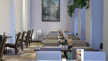 A modern hotel dining area with multiple tables and chairs, a large painting on the wall, and a potted plant.