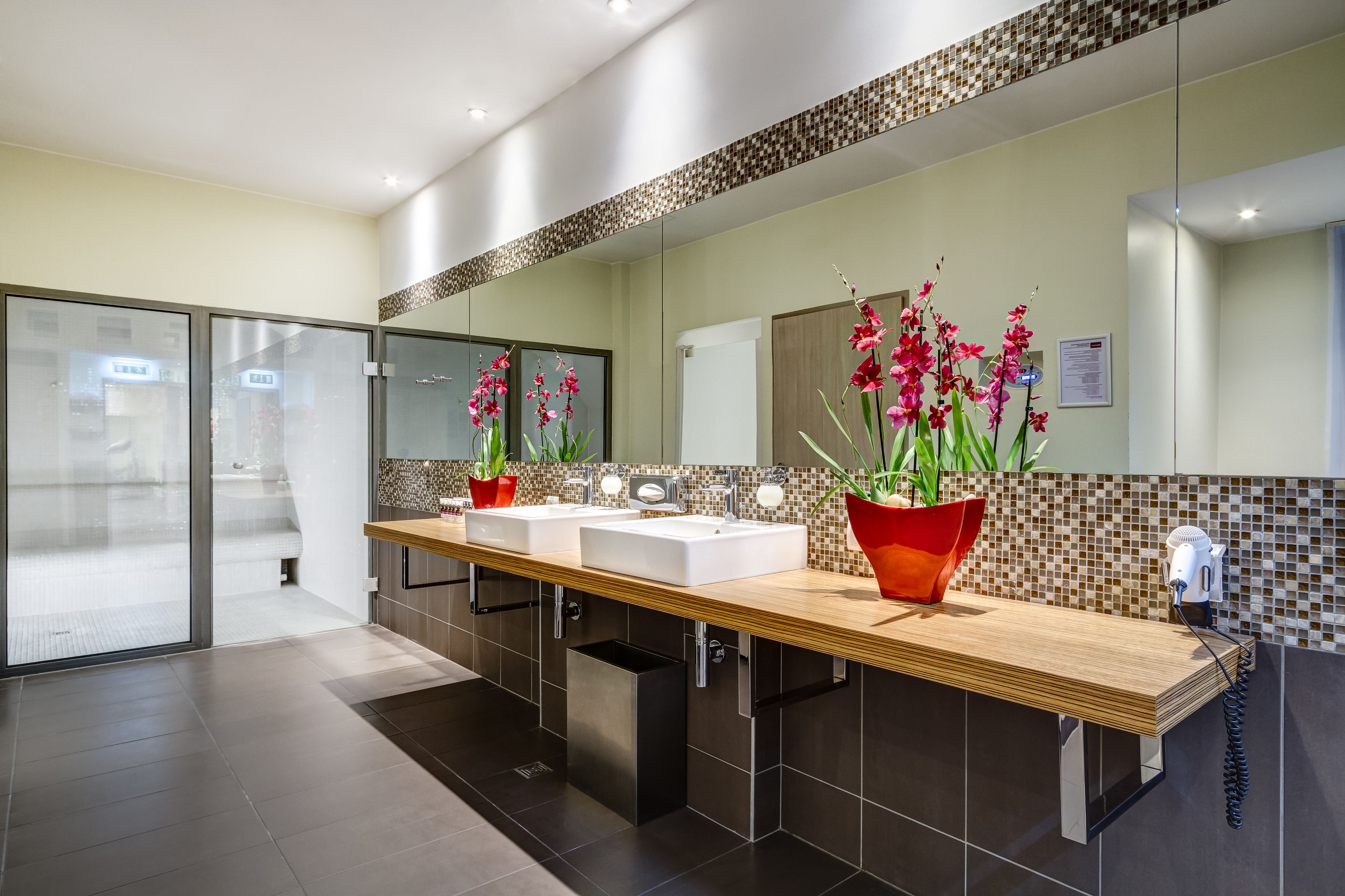 A modern bathroom with a wooden vanity, two sinks, a large mirror, and decorative orchids.