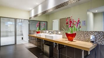 A modern bathroom with a wooden vanity, two sinks, a large mirror, and decorative orchids.