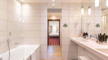 A modern hotel bathroom with a bathtub, a shower, a vanity with toiletries, and a mirror.