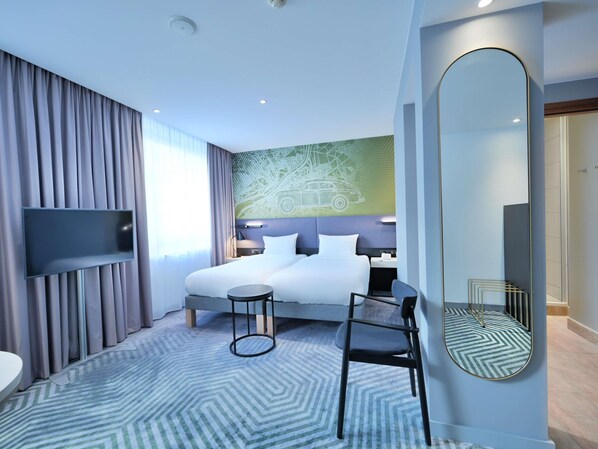 Une chambre d’hôtel moderne, dotée d’un grand lit, d’un bureau, d’une chaise, d’une télévision et d’un grand miroir.