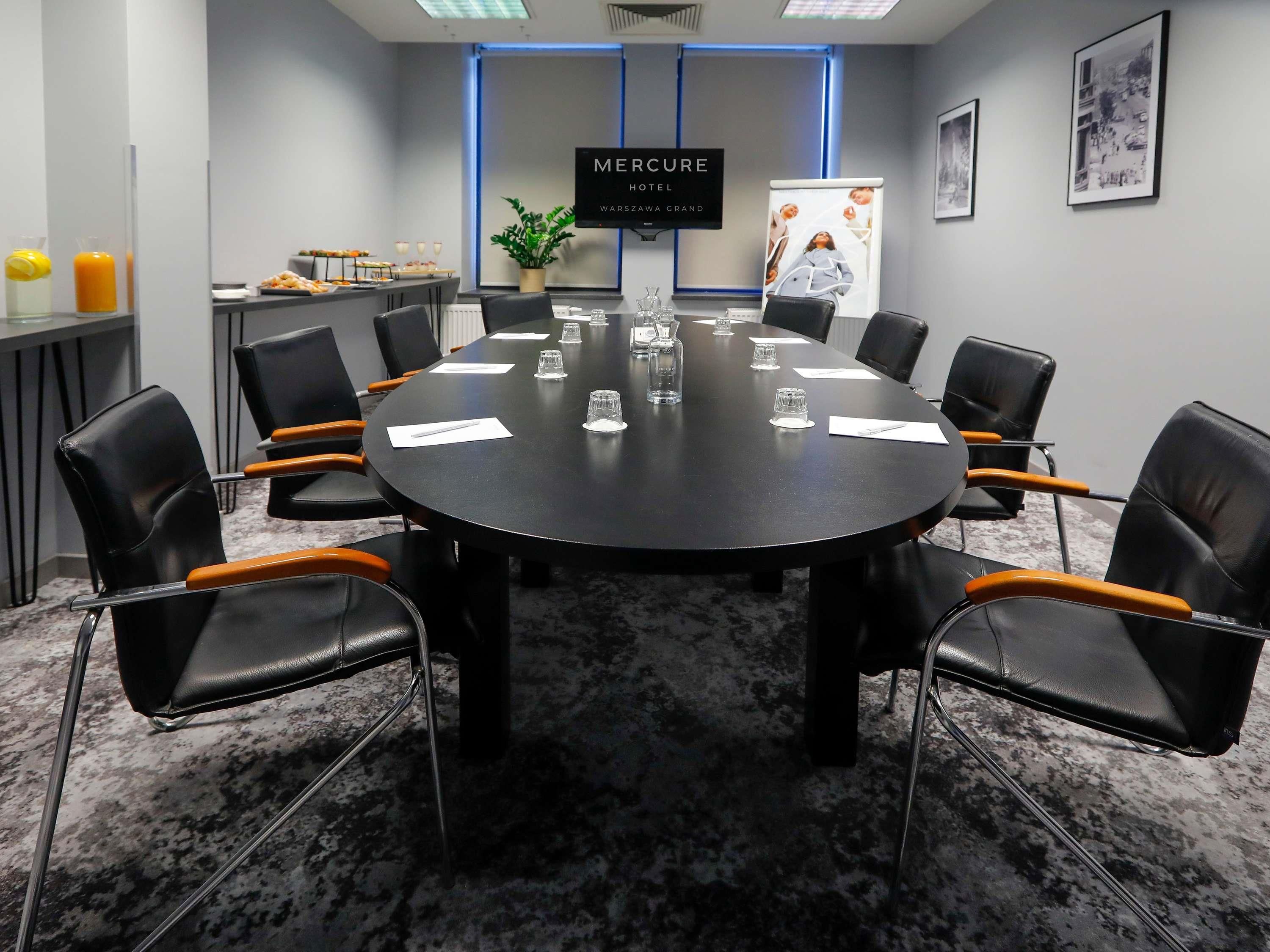 Ein Konferenzraum mit einem runden Tisch, schwarzen Ledersesseln und einem Schild mit der Aufschrift 'Mercure Hotel Warsaw Grand'.