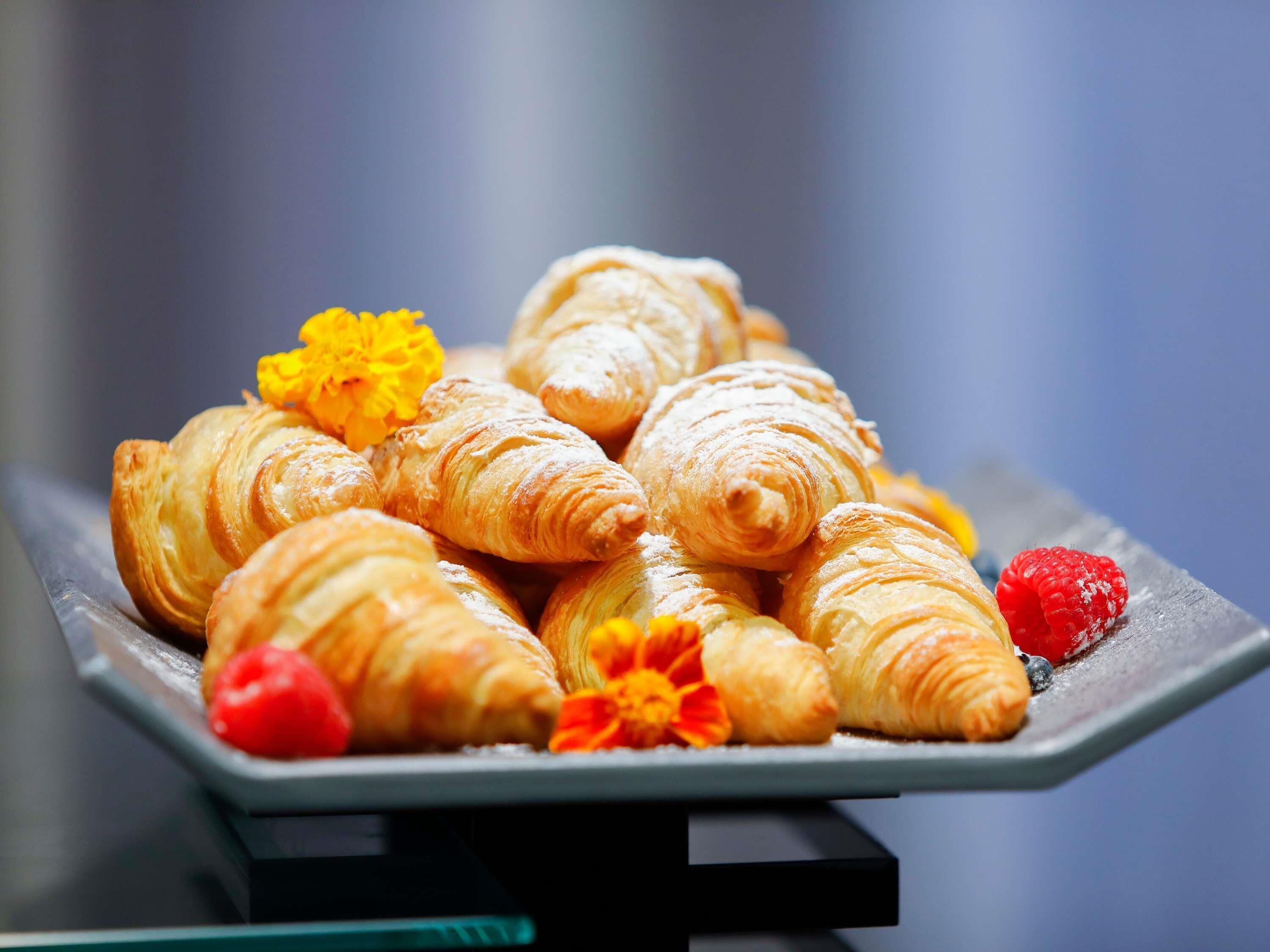 A tray of croissants with a flower and a raspberry.