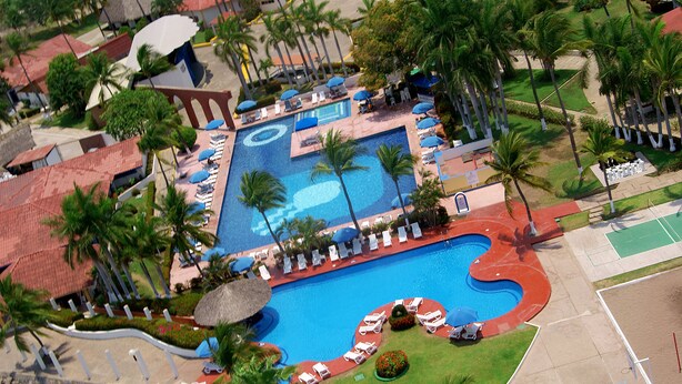 An aerial view of a resort with a central swimming pool, surrounded by palm trees and sun loungers. - Qualton Club Ixtapa - All Inclusive (Ixtapa)
