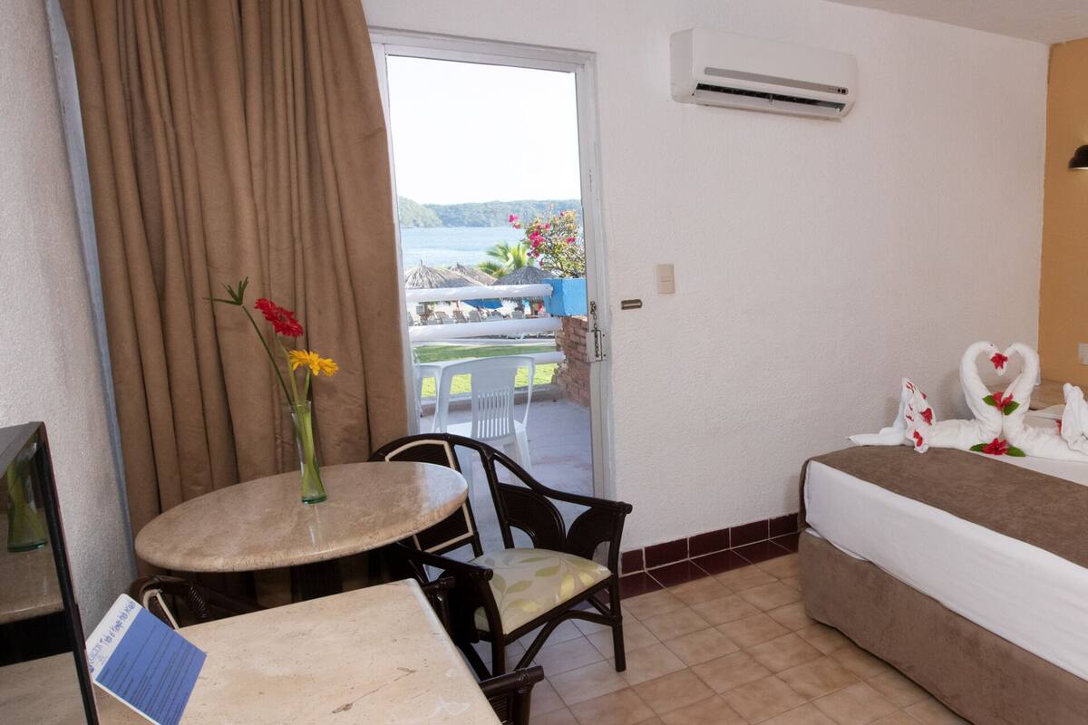 Habitación de hotel con cama, una mesita con una silla, vistas al exterior y un equipo de aire acondicionado.