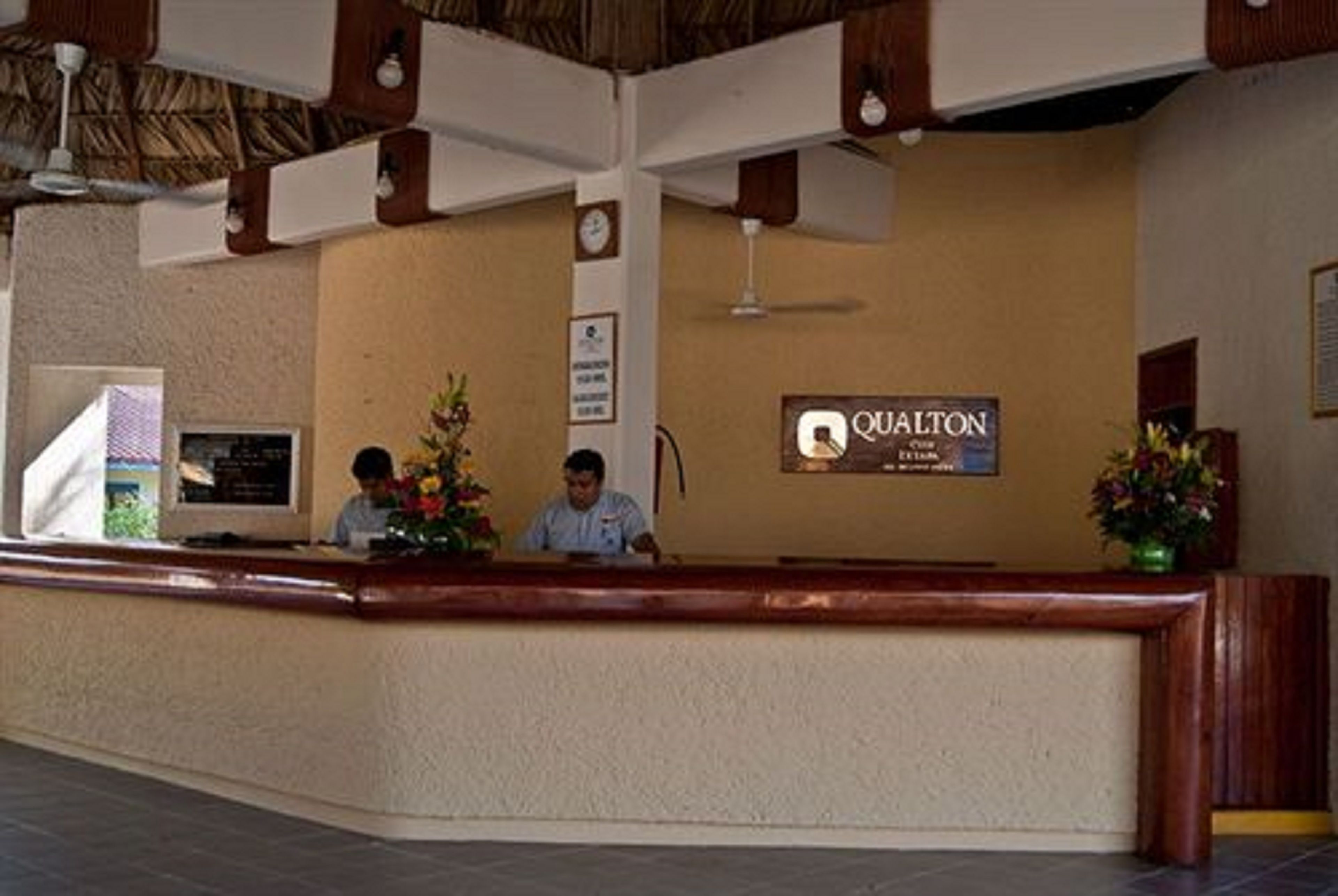 Una recepción con un letrero que dice "QUALTON" y un reloj en la pared.