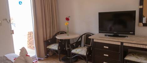A hotel room with a bed, a TV, a small round table with chairs, and a window with curtains.