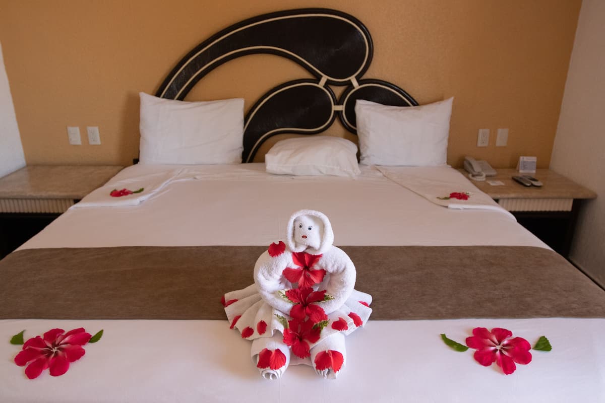 Una habitación de hotel con una cama bien hecha, un cabecero y una mesita de noche con un teléfono y un bloc de notas.